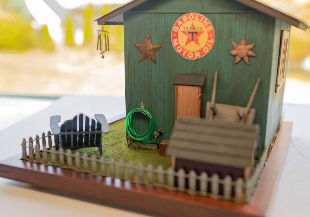 Diorama featuring a green garage with a chair, dog house, hose and other outdoor accessories on a table