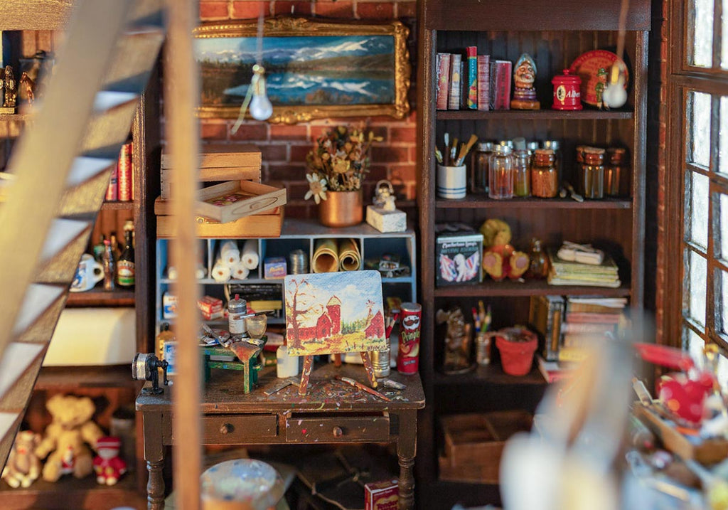 Zoom in view of an artists studio Diorama. A painting is on the table at the centre and painting tools are around it. Many books and decor on the shelf on the background.