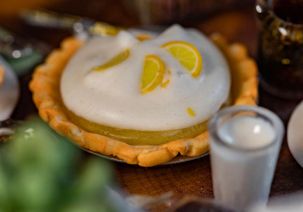 A close up picture of a miniature Lemon Meringue Pie on a table next to a glass of water